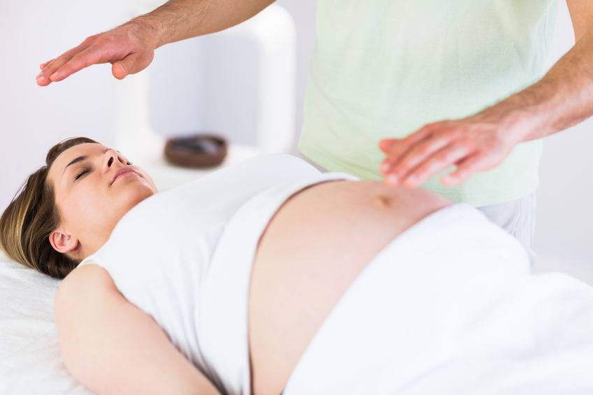 Relaxed pregnant woman getting reiki treatment in a studio